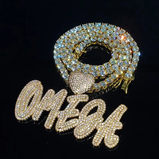 Gold iced out custom name pendant with brush script lettering on a Cuban link chain, black background