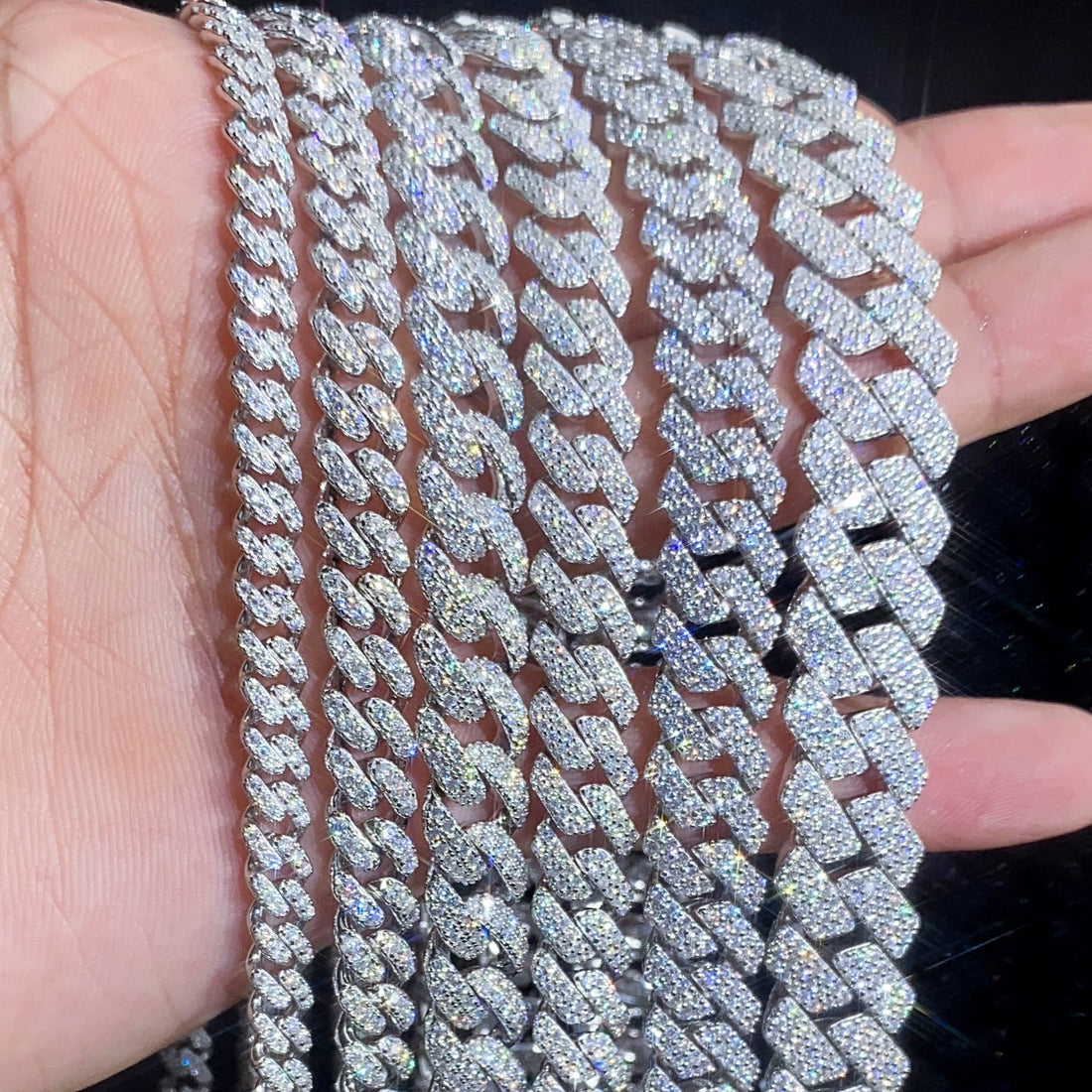 Multiple iced out Cuban link chains in different widths held in hand — silver CZ cuban chain size comparison 9mm to 20mm
