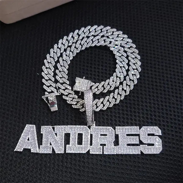 Iced out silver Cuban chain with custom CZ nameplate pendant spelling ANDRES on black background