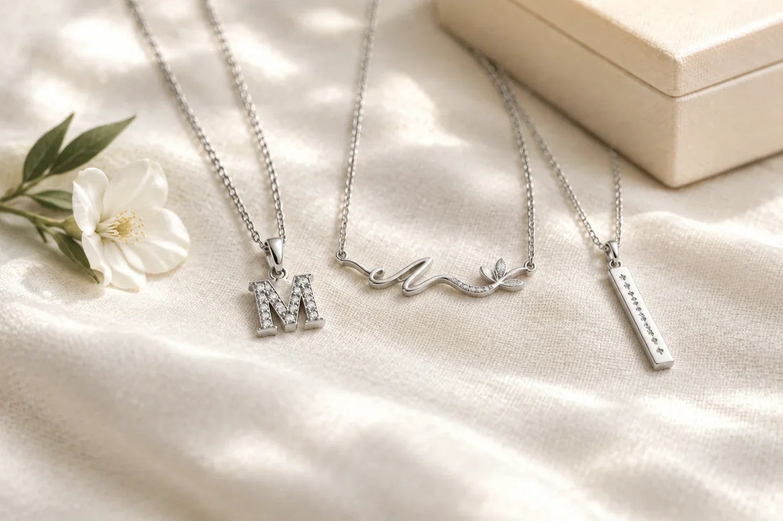 Silver mother memorial necklaces with initial, nameplate, and date charms on ivory linen